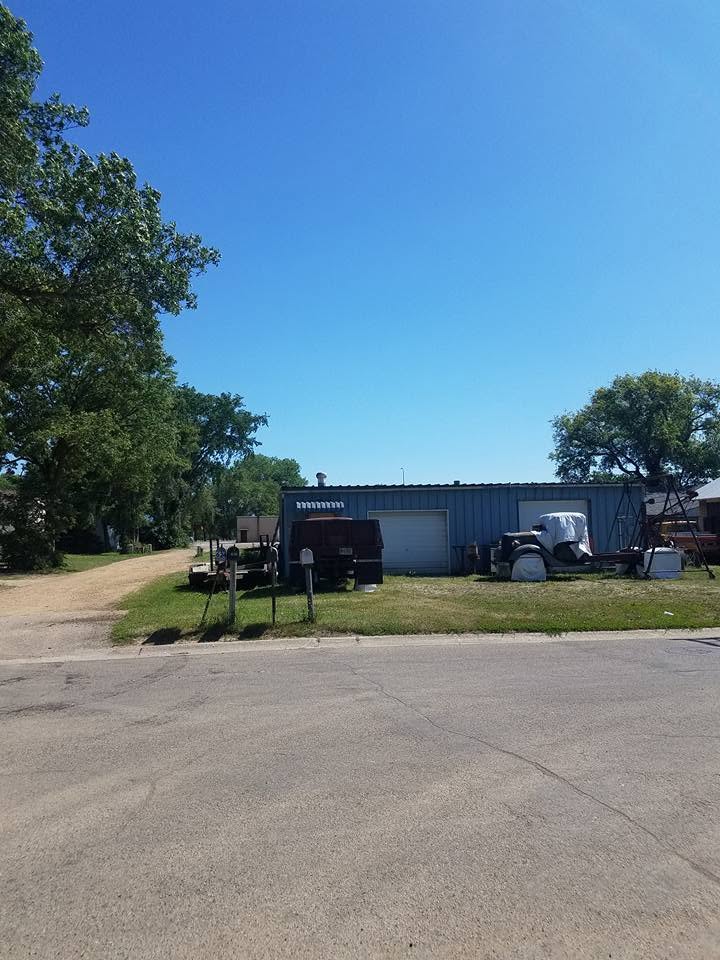 The same blue metal shop building with the large tree removed, open sky where it stood